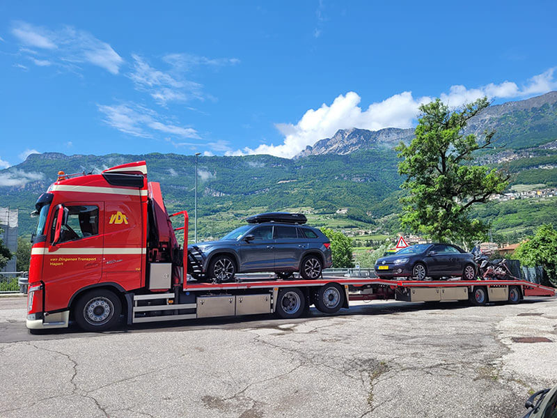 Lastkraftwagen mit zwei Autos und einem Motorrad auf einem Anhänger